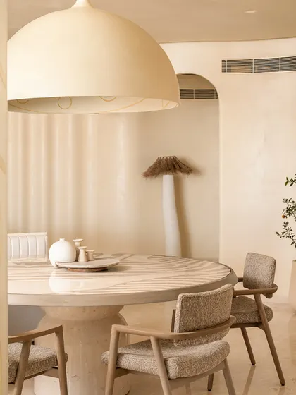 The dining area in Soft Serve, where a monolithic stone table is surrounded by comfortable upholstered chairs, all under a large dome pendant light.