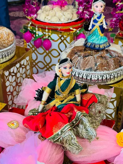 A doll dressed in a rich red and green saree, seated elegantly on a pink lotus base. This kind of arrangement adds a pop of color and sophistication to any platter display.