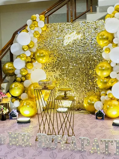 A straight-on view of the gold sequin wall setup. The combination of the shimmering backdrop, neon sign, and balloon garland creates a rich, textured look.