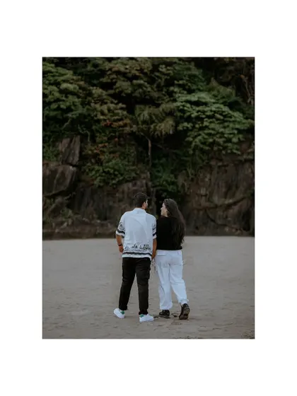 A shot from behind as the couple stands on the beach, looking towards the lush green cliffs, symbolizing the adventures that lie ahead.