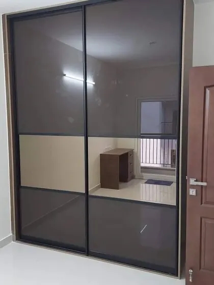 A beautifully designed lacquered glass sliding wardrobe. The two-tone design with a metallic frame adds a touch of modern sophistication to the bedroom.