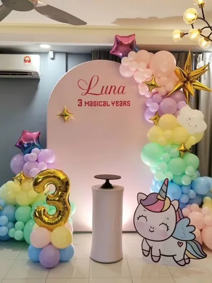 Celebrating '3 Magical Years' with a pastel unicorn and rainbow theme. This home setup includes a pink arched backdrop, cloud-like balloon arrangements, and a golden number '3' foil balloon.