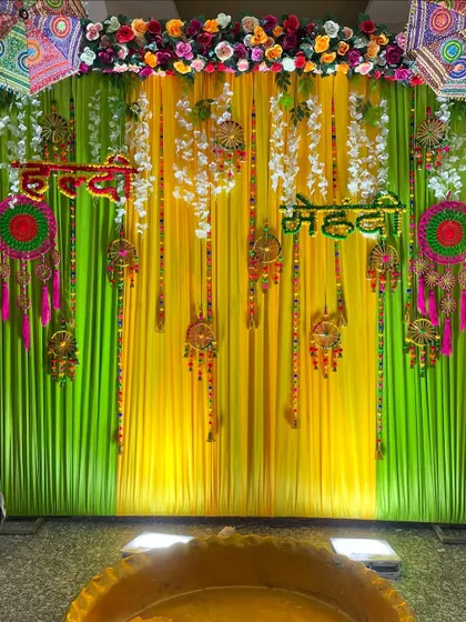 A detailed shot of the upper portion of the Haldi-Mehendi backdrop, highlighting the floral border, embroidered umbrellas, and hanging decorations.