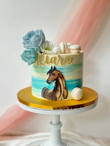 An elegant horse-themed cake with a painted horse portrait. The watercolour-style buttercream and delicate sugar flowers give it an artistic and sophisticated feel.