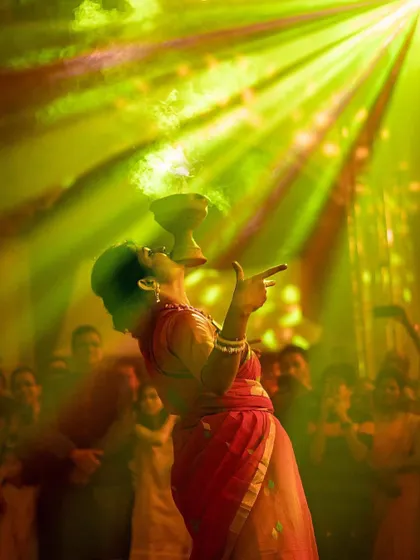 A woman performs a traditional dance at a celebration, balancing a smoking vessel in her mouth under dramatic yellow stage lights. This captures the energy and cultural richness of a live event.