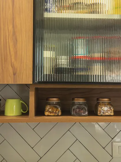 This close-up highlights the material details: fluted glass on an overhead cabinet, open shelving for spices, and the texture of the herringbone tiles.