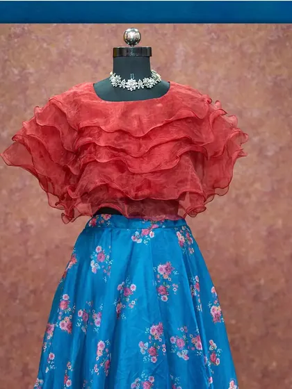 A modern crop top and skirt set, featuring a floral blue skirt and a layered red organza top.