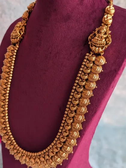 A detailed shot of the long Kaasu haara, featuring the embossed Lakshmi coins and the larger deity pendant. This piece adds length and grandeur to a bridal look.