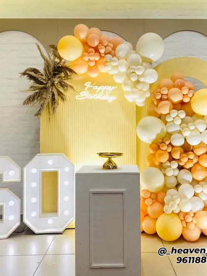 A chic and modern setup for a 60th birthday celebration. This design uses a sophisticated color scheme of peach and white balloons, large light-up marquee numbers, a neon "Happy Birthday" sign, and dried pampas grass for an elegant touch.