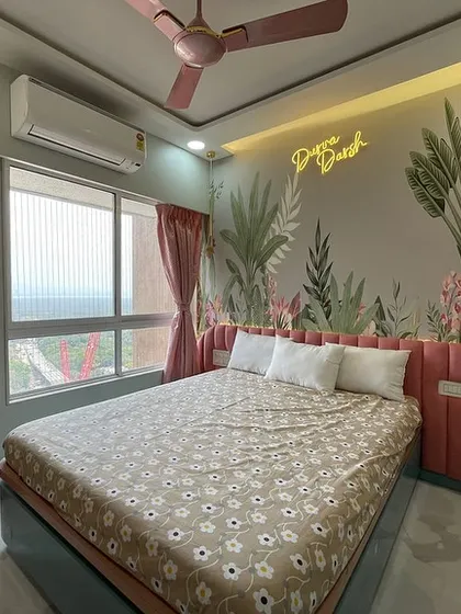 A whimsical bedroom featuring a tropical-themed wallpaper and a neon sign that reads "Dream Big." The pink upholstered headboard and matching curtains create a soft and playful atmosphere.