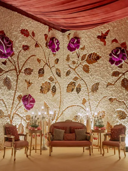 This magnificent stage backdrop is a custom-made flower wall, with a base of white carnations and a design of climbing roses made from purple and metallic-gold dyed petals.