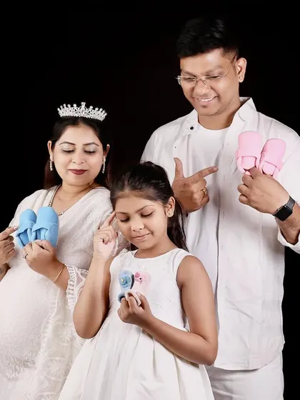 A fun gender reveal concept for a family. The parents and their daughter hold up blue and pink baby shoes, playfully guessing and celebrating the new baby on the way.
