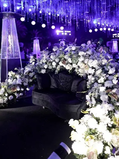 We create stylish and comfortable lounge areas for guests to connect. This chic seating arrangement, enveloped in white florals and set under dramatic purple lighting, provides a sophisticated space for networking at a corporate cocktail party.