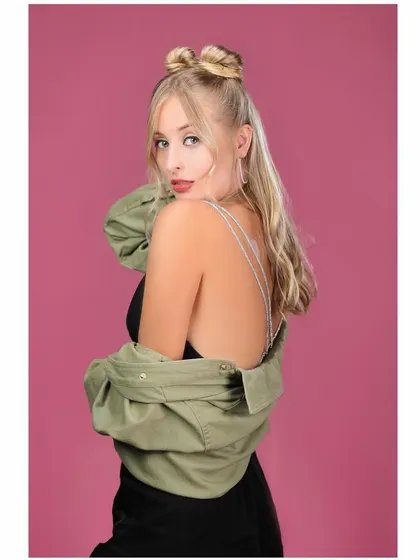A fun and stylish portrait against a pink background. The pose is playful and confident, and the green jacket adds a nice color contrast.