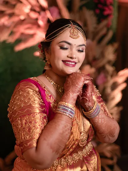 A sweet and adorable close-up of a South Indian bride, her hands clasped and a happy smile on her face.
