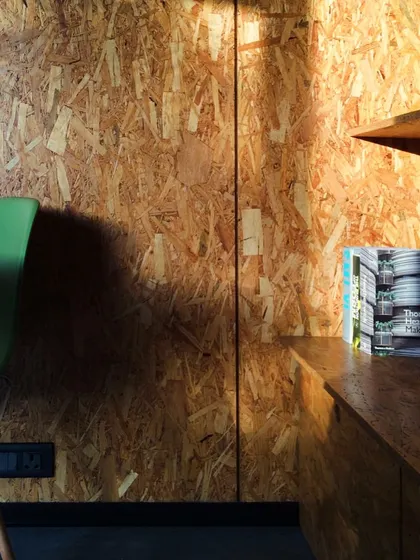 An interior detail of the journalist's workspace, showing the rich texture of the OSB walls and the simple, functional built-in shelving. The design is minimalist yet highly practical.