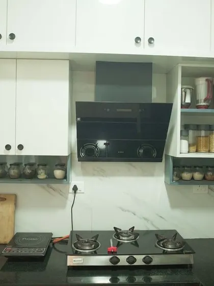 This L-shaped kitchen features a combination of white and grey cabinets with a marble-effect backsplash. The design is part of a full 3BHK interior project, ensuring a cohesive look throughout the home.