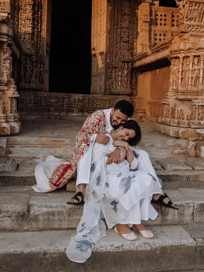 A tender and joyful moment on the steps of an ancient temple. The groom's colorful shawl adds a vibrant touch to their coordinated white outfits.