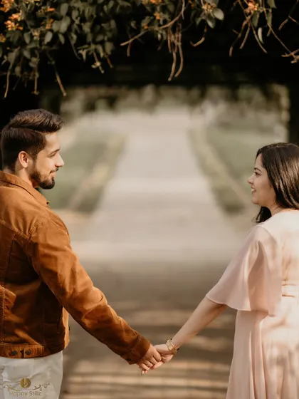 A couple holds hands, looking towards each other down a tree-lined path. The symmetry and leading lines of the path create a beautiful composition that draws you into their world.