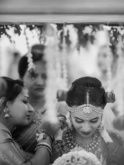 A candid black and white shot of the bride's entry. The focus is on the quiet, emotional moments between family members just before the main ceremony.