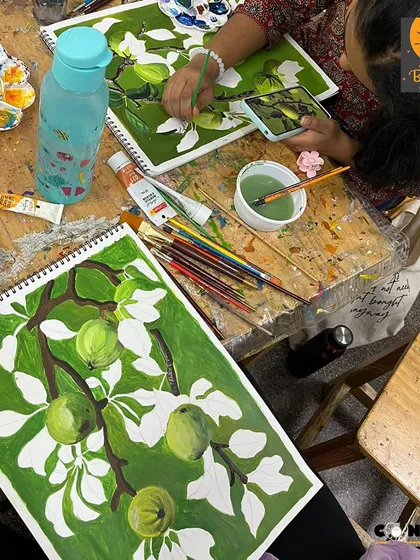 An aerial view of the studio table shows two students working on the same monochrome apple branch project, each developing their own unique brushwork.