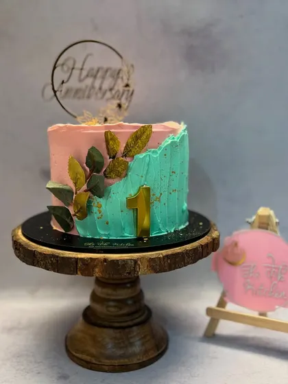 A lovely anniversary cake with a two-tone buttercream finish in pink and teal. The golden leaves add a touch of elegance to the design.