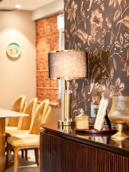 A sneak peek into the dining room, focusing on the details of the console area. The warm lighting from the table lamp creates a cozy and inviting atmosphere, highlighting the textures of the wallpaper and fluted cabinet.
