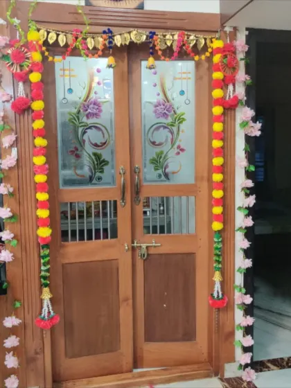 A beautifully decorated main door to welcome guests for a celebration. The setup includes a traditional toran, marigold garlands, and artificial flower vines.
