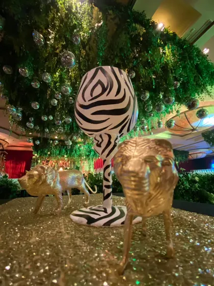 A giant zebra-print wine glass and golden animal figures create a fun and surreal centerpiece on a glittering gold table.