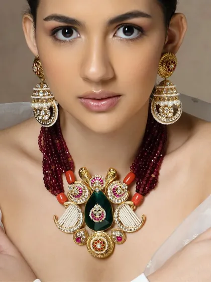 A majestic piece featuring a large teardrop-shaped emerald, surrounded by intricate polki work and set on a string of ruby beads.
