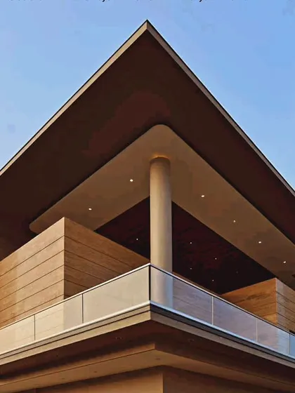 A detail of a modern balcony on a commercial building. The design uses a sharp, angular roofline, a single supporting column, and wood-paneled volumes to create a sophisticated and sheltered outdoor space.