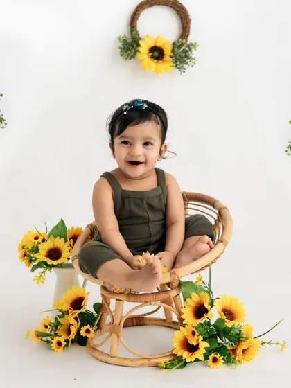 A sunny sunflower-themed first birthday! This happy baby is surrounded by bright yellow flowers, sitting in a cute rattan chair for her milestone portrait.