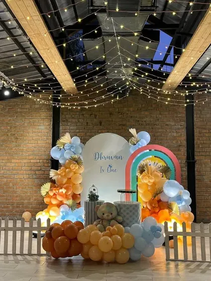 A charming Teddy Bear theme for a first birthday in a hall with high ceilings, featuring fairy lights and a rainbow-accented backdrop.