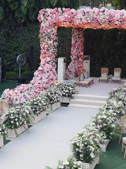 A wide view of the magnificent floral mandap and guest seating. The aisle is lined with arrangements of white and pink flowers, creating a beautiful path for the bride.