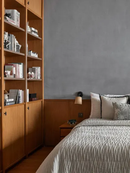 Designed as a personal retreat for a resident who loves reading, this bedroom features a wall of custom bookshelves. The muted blue-grey stucco wall provides a calming backdrop to the warmth of the wooden paneling and book collection.