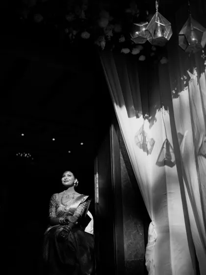 A black and white portrait of a bride, her face illuminated by a soft light from the side. The shadows and her thoughtful expression create a timeless and emotional image.