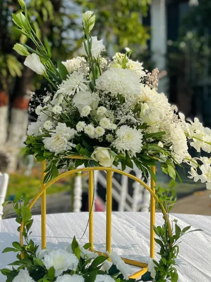 A beautiful centerpiece for a white-themed wedding. A simple arrangement of white orchids and other blooms in a golden stand adds a touch of sophistication to the guest tables.