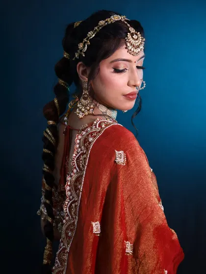 This elegant bridal look features a long, decorated braid and a beautiful matha patti. The side profile highlights the intricate hairstyle and the soft, glowing makeup.
