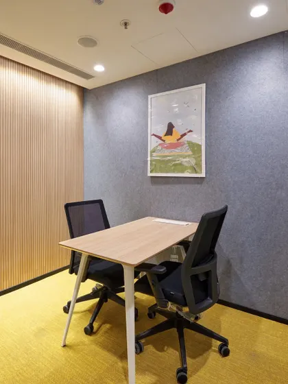 We create functional "huddle rooms" for private conversations or focused work. This space uses acoustic wall panels for soundproofing, a simple table setup, and a bold yellow carpet to add a touch of energy.