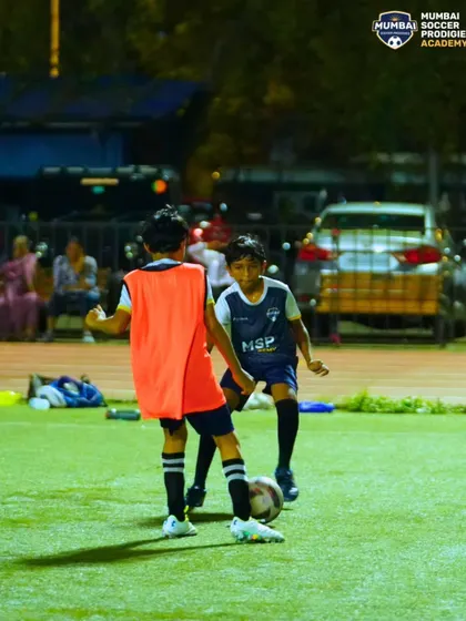 Two players in a 1v1 drill, learning to shield the ball and maintain possession under pressure.