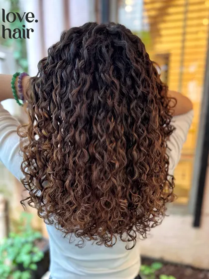 Adding dimension with a brunette balayage. These lighter pieces are strategically placed to catch the light and make the curls pop without a full head of colour.