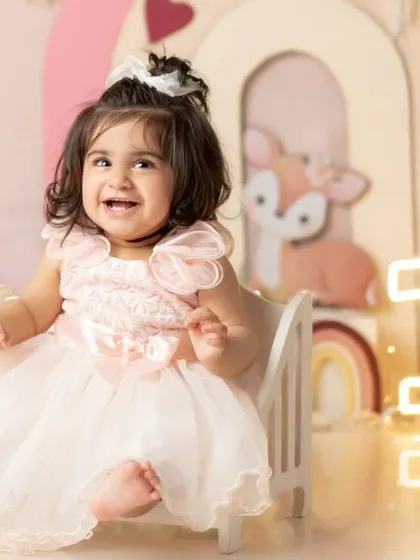 A princess in her throne. This little one is all smiles in her beautiful pink dress, celebrating her first birthday.