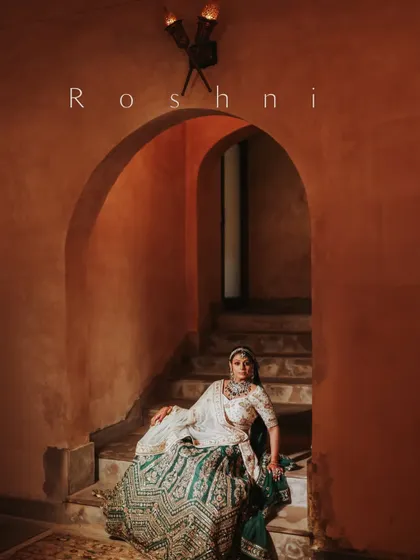 A royal bridal portrait. The bride is seated on a staircase in a palace, her intricate lehenga and regal pose creating an image of timeless elegance.