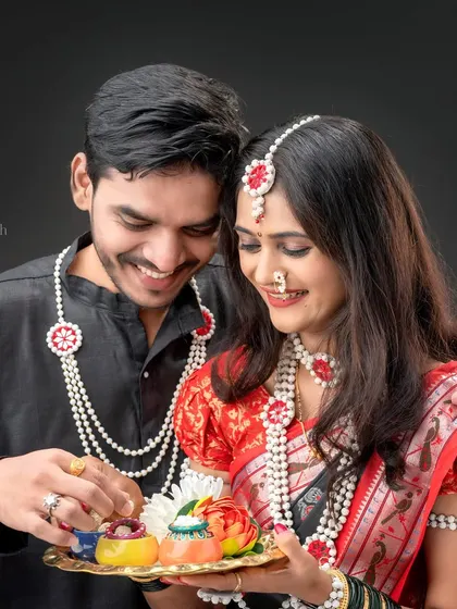A candid moment between a couple during their festive shoot. The husband playfully interacts with the items on the thali held by his wife, creating a natural and sweet memory.