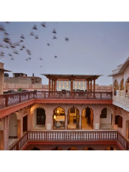 An atmospheric shot of the Haveli Dharampura courtyard and terrace, capturing a flock of birds in flight. This image, featured by EconomicTimes.com, highlights the haveli as a hidden gem for travelers.