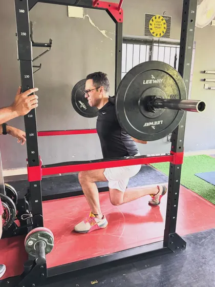 A client performs a barbell split squat in a rack, a setup that allows for heavy loads while maintaining safety.
