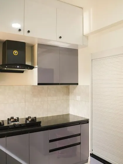 This L-shaped kitchen features glossy grey cabinets with sleek black profile handles. The design includes a mix of open and closed storage, with glass-fronted cabinets and a dedicated spice rack for convenience.