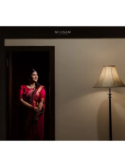 A portrait of the bride during her Pindhani ritual, standing in a doorway. The simple composition and warm lighting create a feeling of quiet elegance and anticipation.