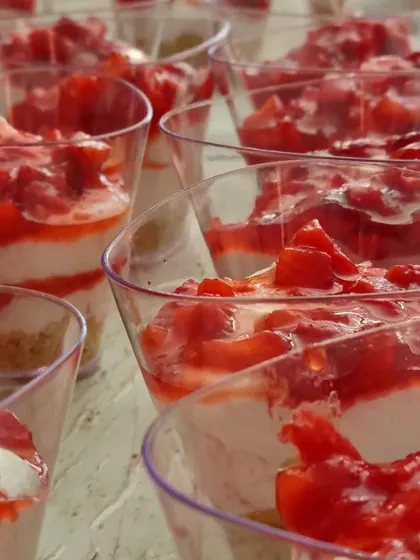 A close-up of our strawberry cheesecake cups, ready to be served. The layers of biscuit, cream cheese, and fresh strawberry compote are visible through the clear cups.