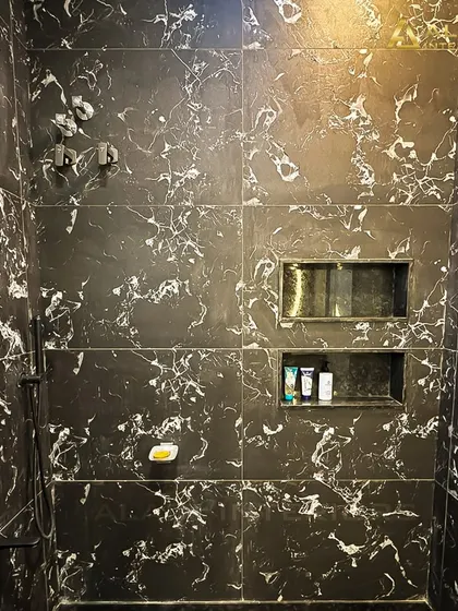 A close-up of a shower area fully tiled in a striking black marble with white veining. The built-in niches provide convenient storage for toiletries.